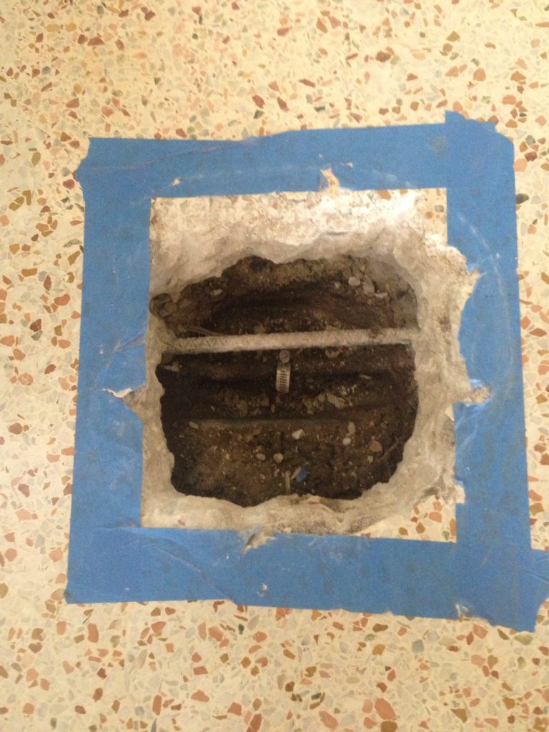 Opening cut in a terrazzo floor and outlined in blue tape to reach a slab leak