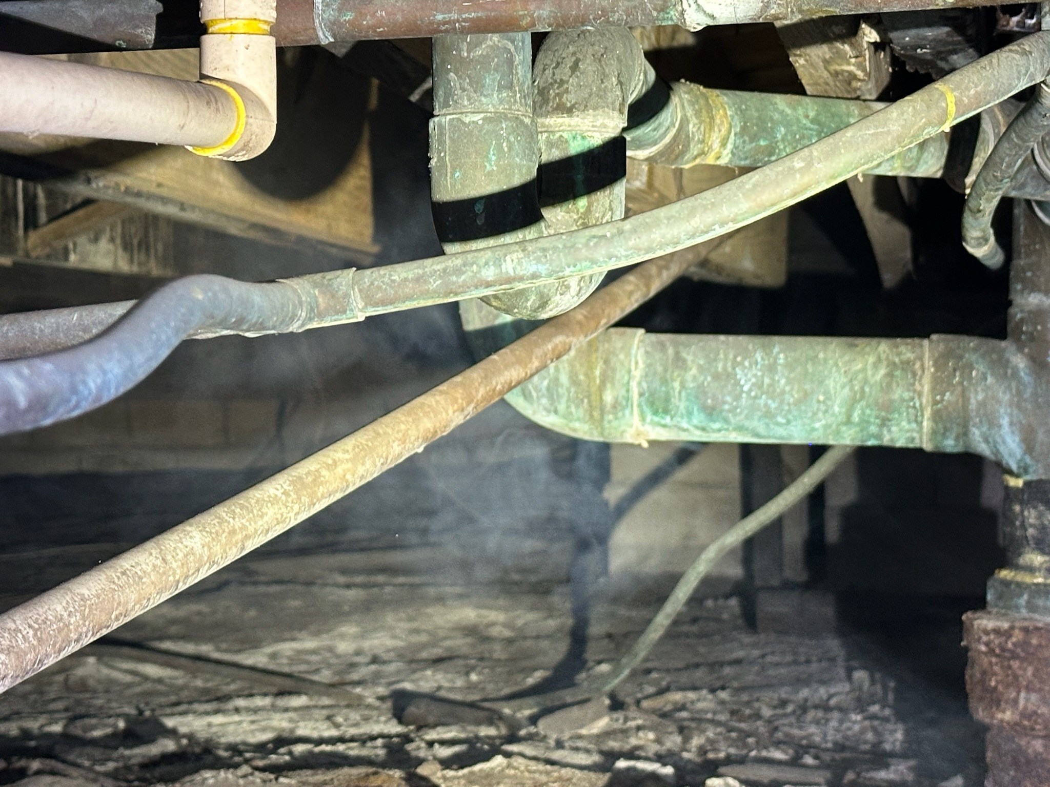 Smoke mist visible in a crawlspace around a cast iron pipe transitioning to copper during a sewer odor test.