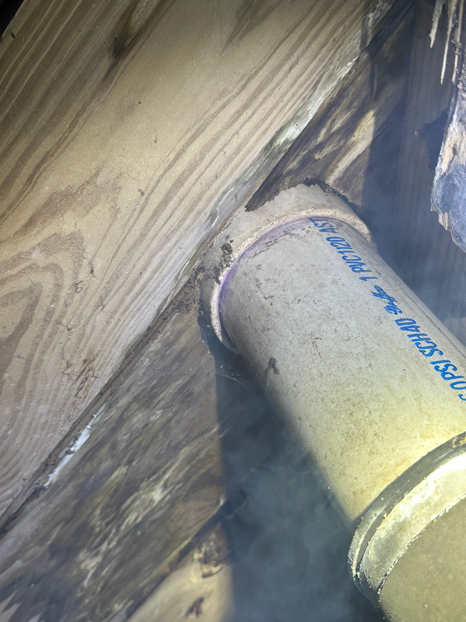 White smoke escaping from behind a PVC pipe entering the floor, showing the rodent entry point into the home.