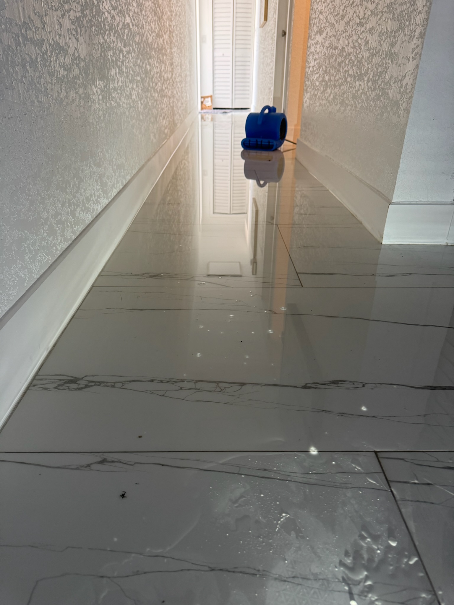 Flooded marble tile hallway in Madeira Beach home with standing water reflecting light