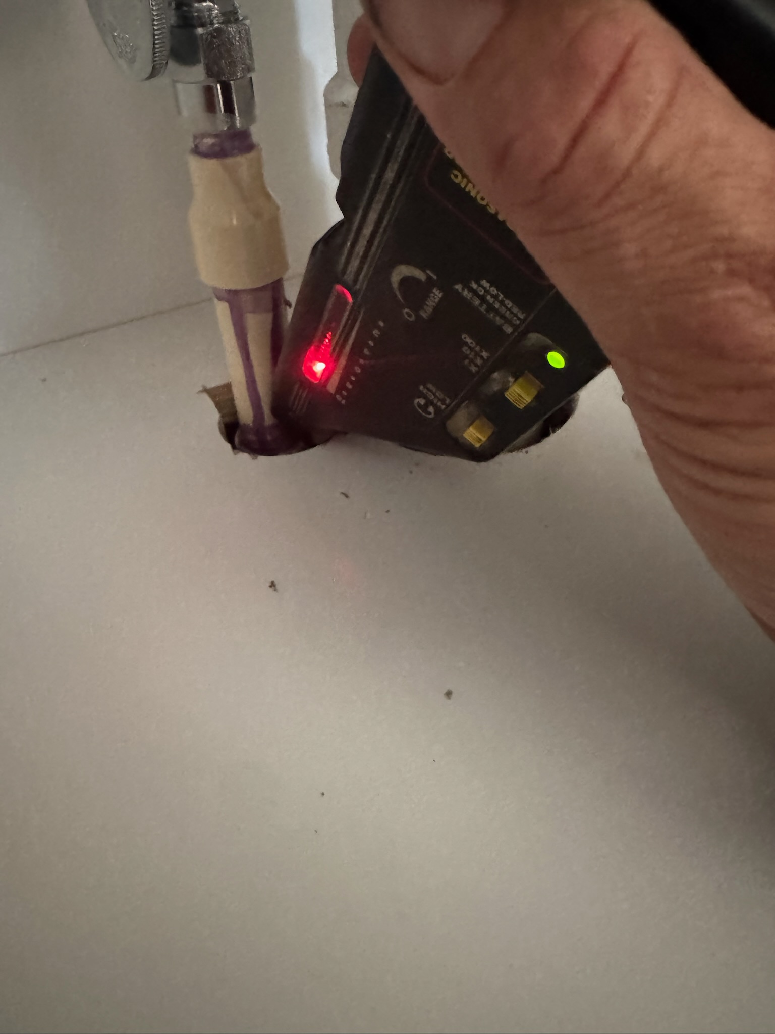 Leak detection device aimed at CPVC pipe with visible angle stop under sink in Oldsmar kitchen