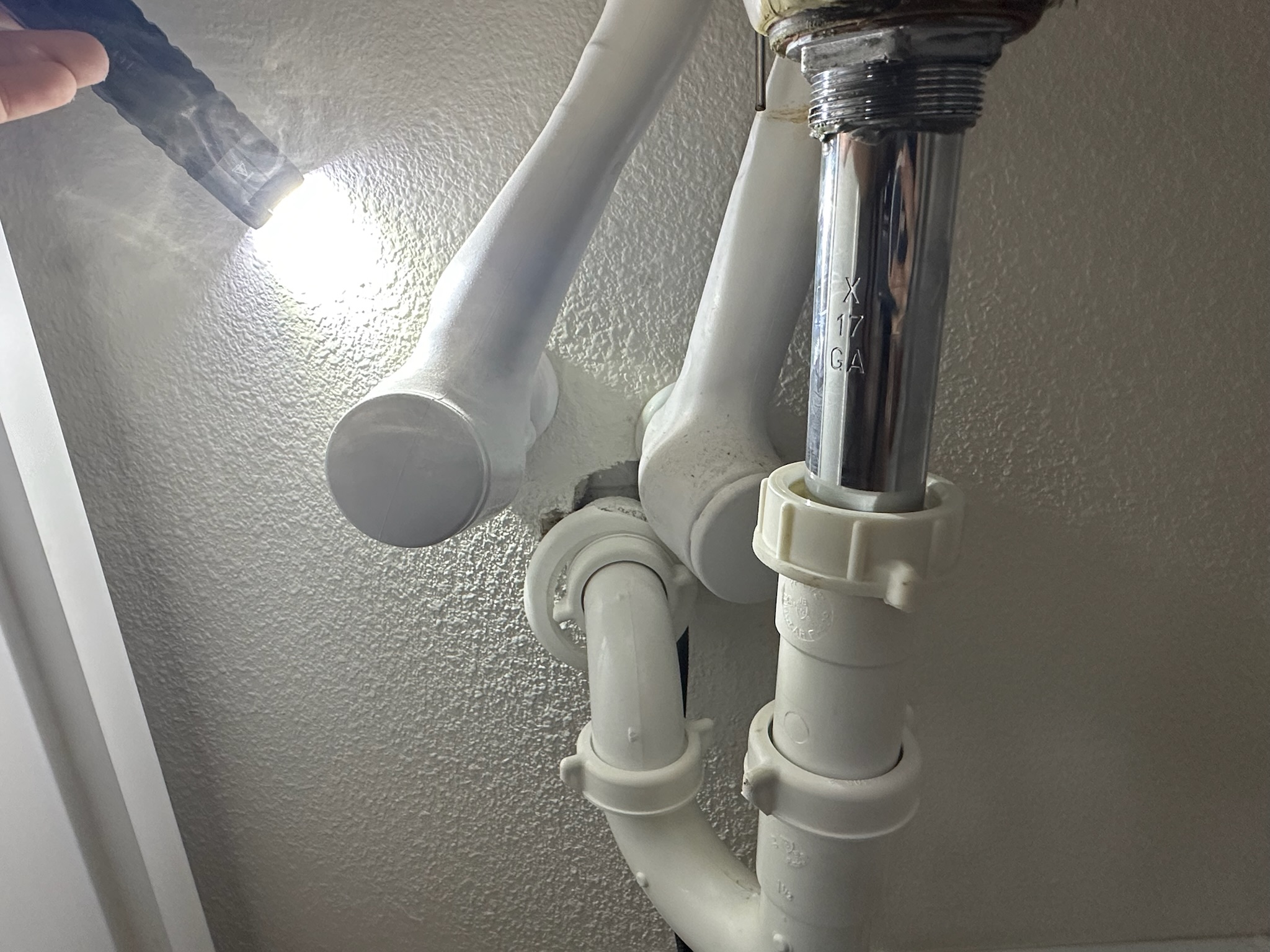 Technician using flashlight to inspect sewer odor leak with smoke emerging from wall near sink in Palm Harbor.