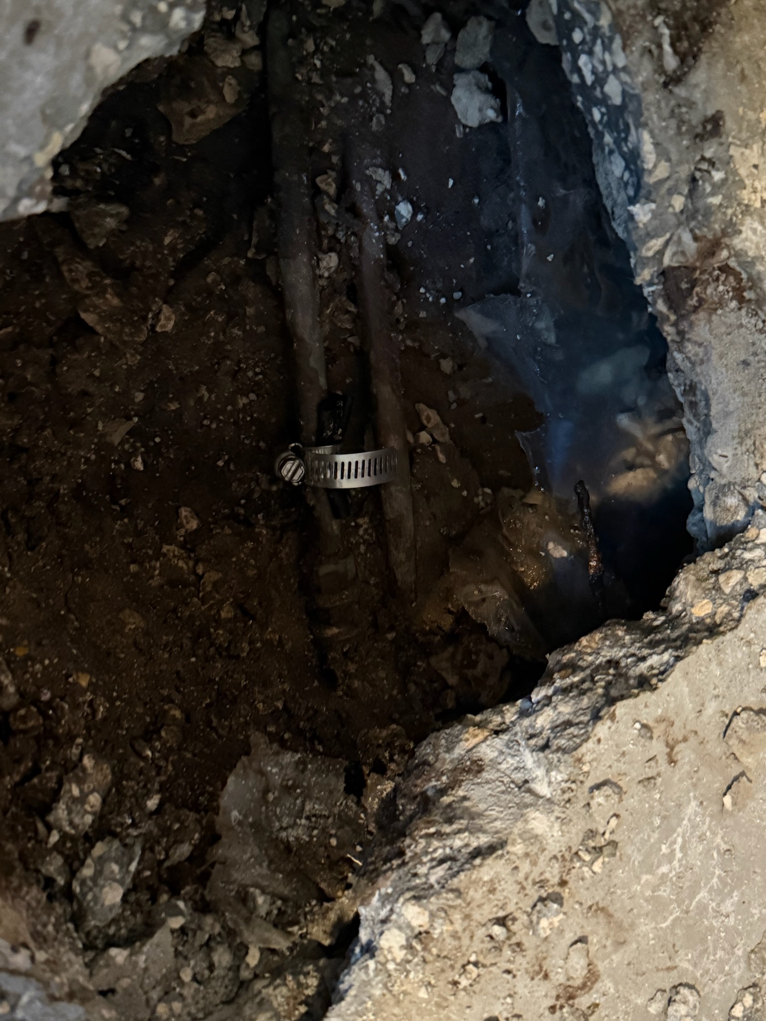 Close-up of two copper pipes under slab with clamp visible on leaking pipe