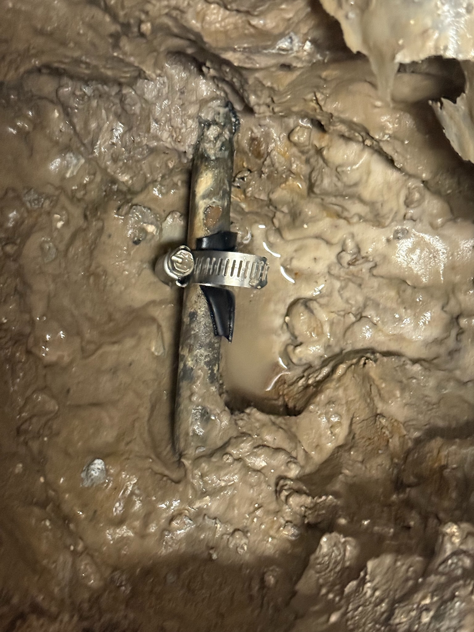 Close-up of copper pipe with bicycle tube and clamp repair in muddy water under slab