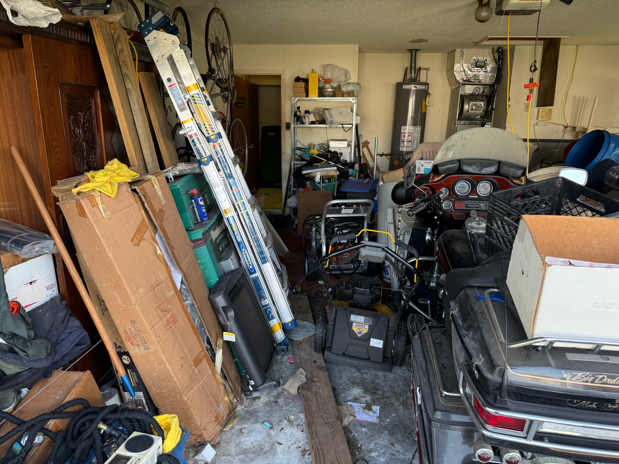 Cluttered garage with boxes stacked on a Harley motorcycle and bicycles hanging from the ceiling