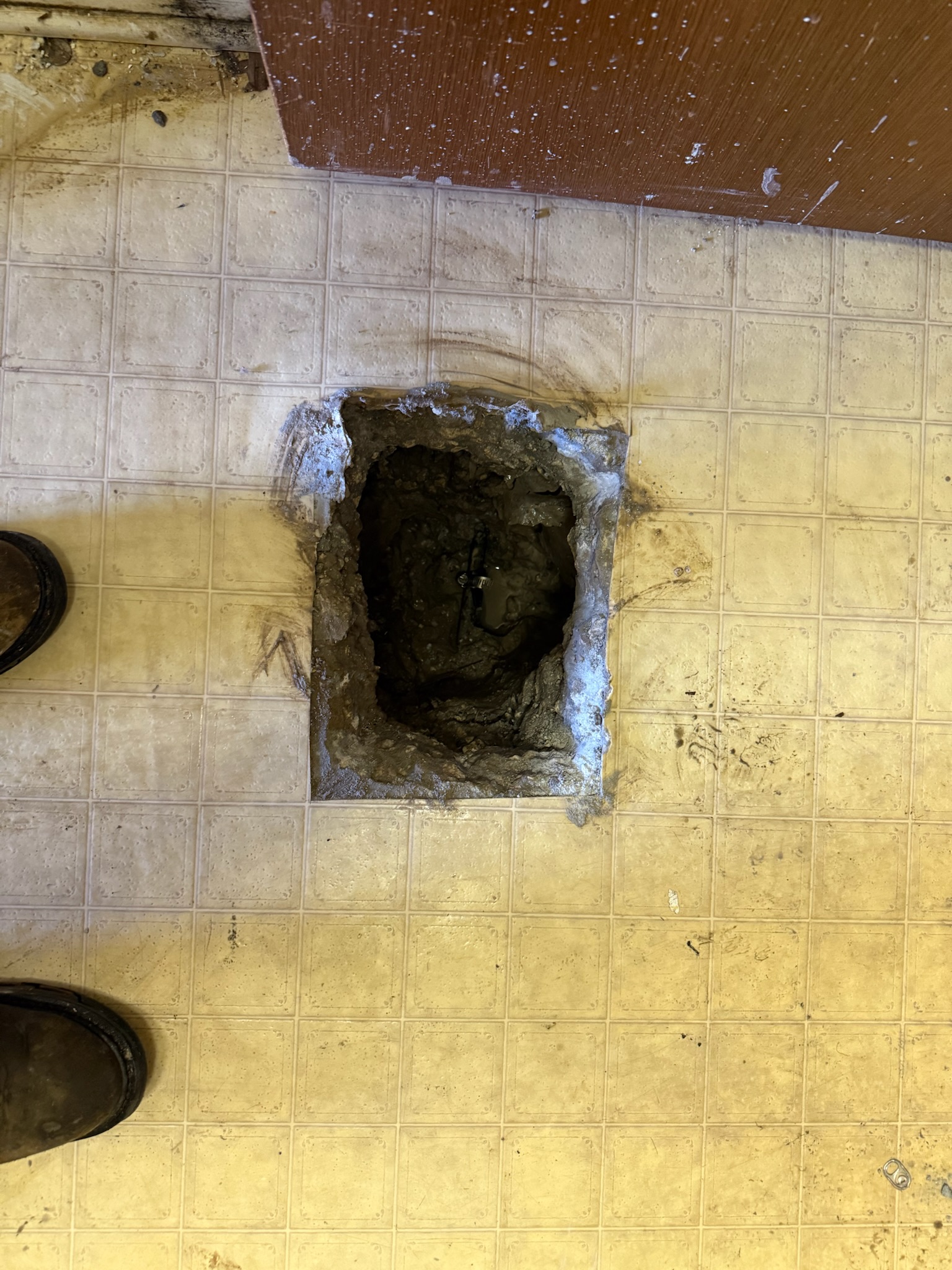 Close-up of exposed slab leak directly centered in small cut-out section of flooring