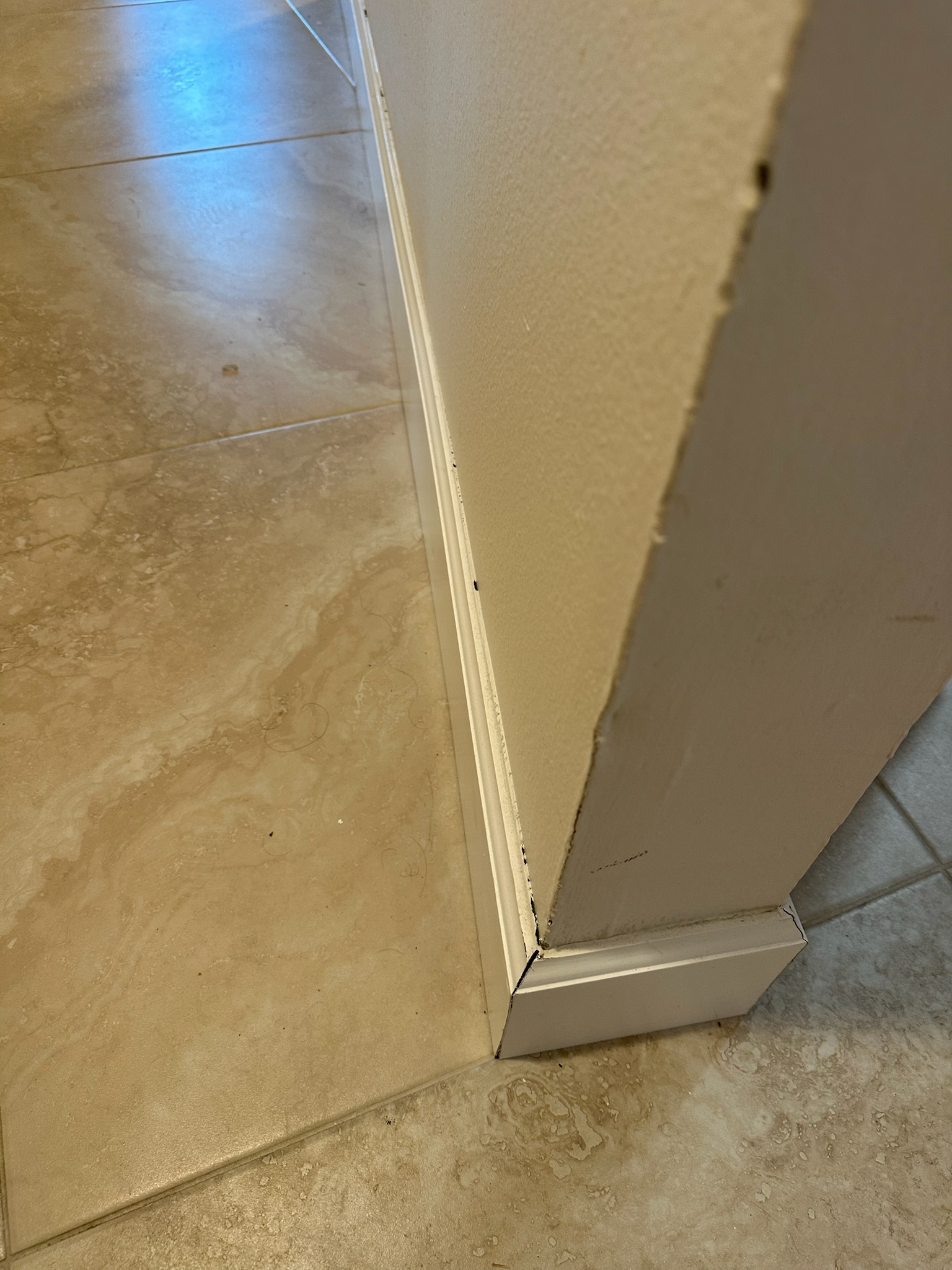 Baseboard peeling slightly from a brown painted wall with tile flooring in a Westchase home.