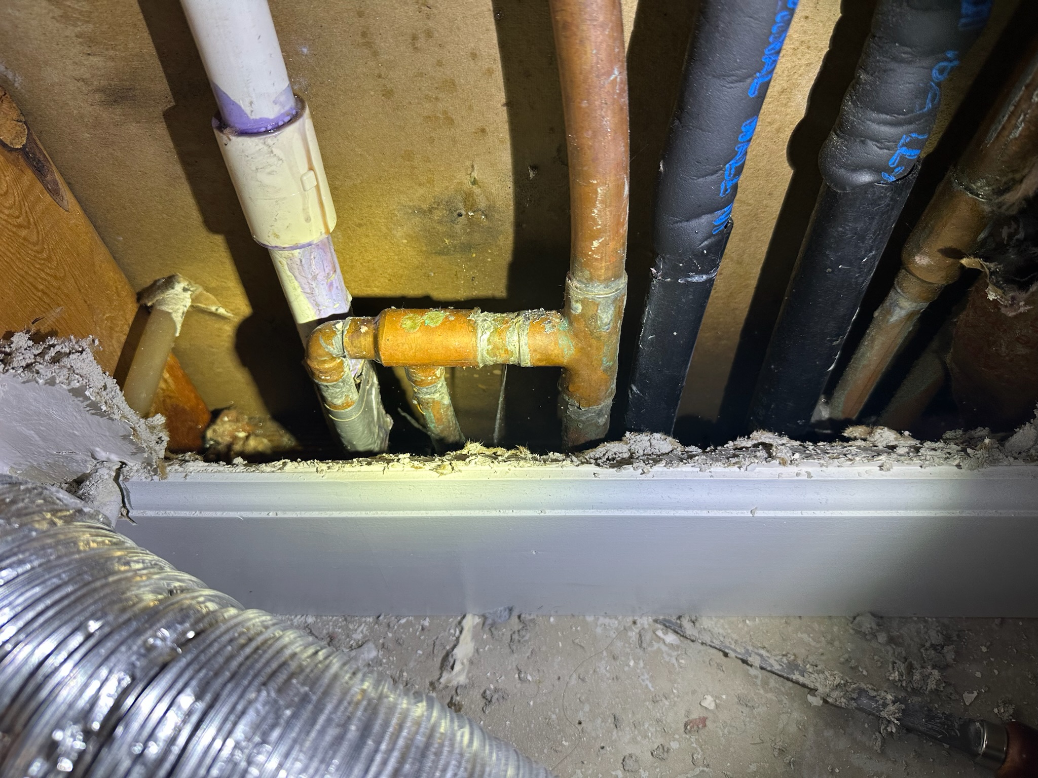 Water spraying from a copper manifold pipe behind a dry tile wall and baseboard in a Westchase home.