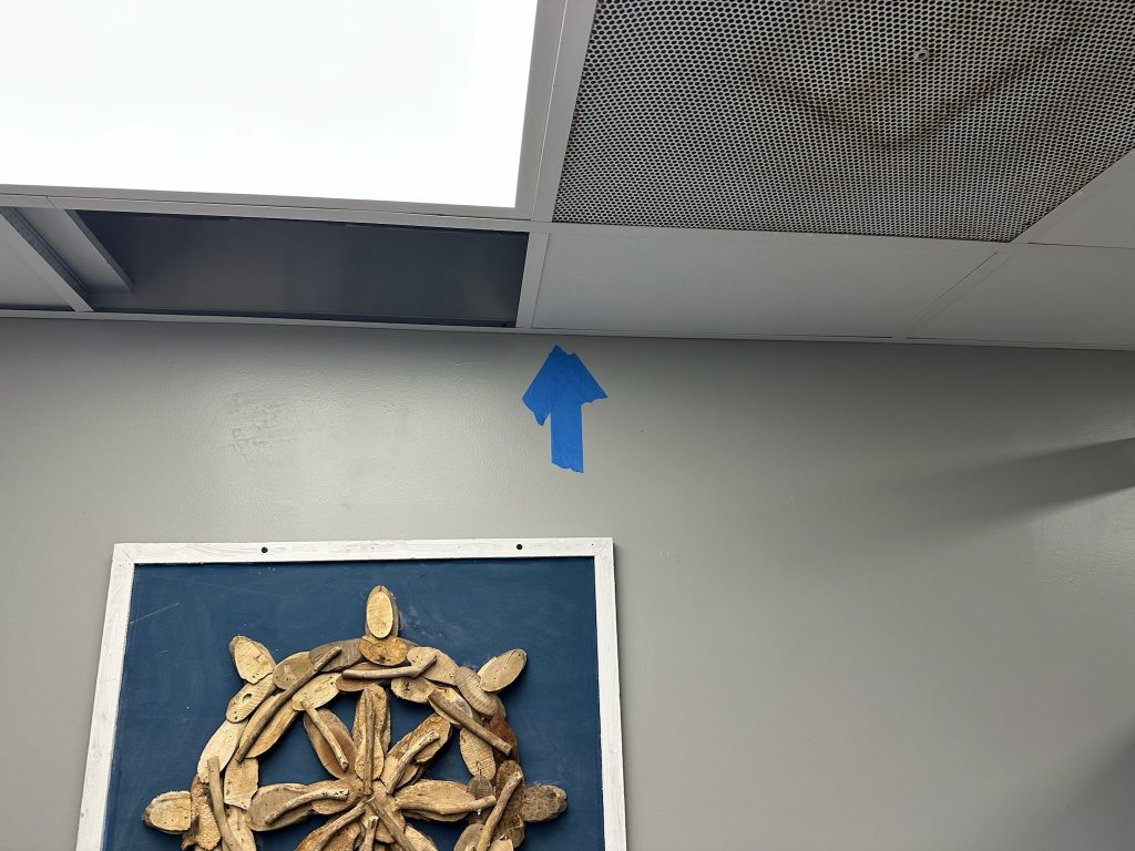 Blue tape arrow marking sewer odor leak location above restaurant ceiling
