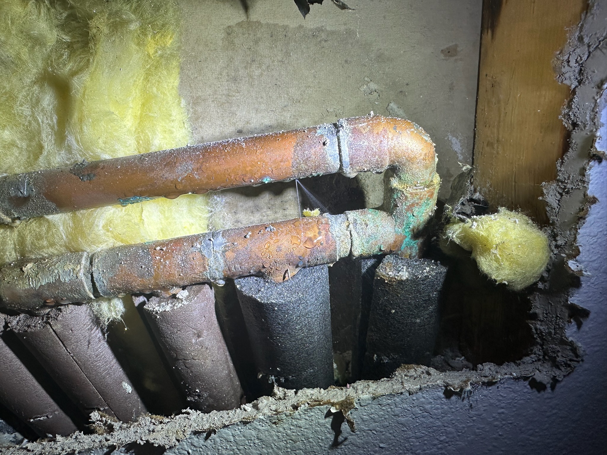 A pinhole leak sprays from a copper pipe above a copper manifold inside the wall, not under the slab as originally suspected.