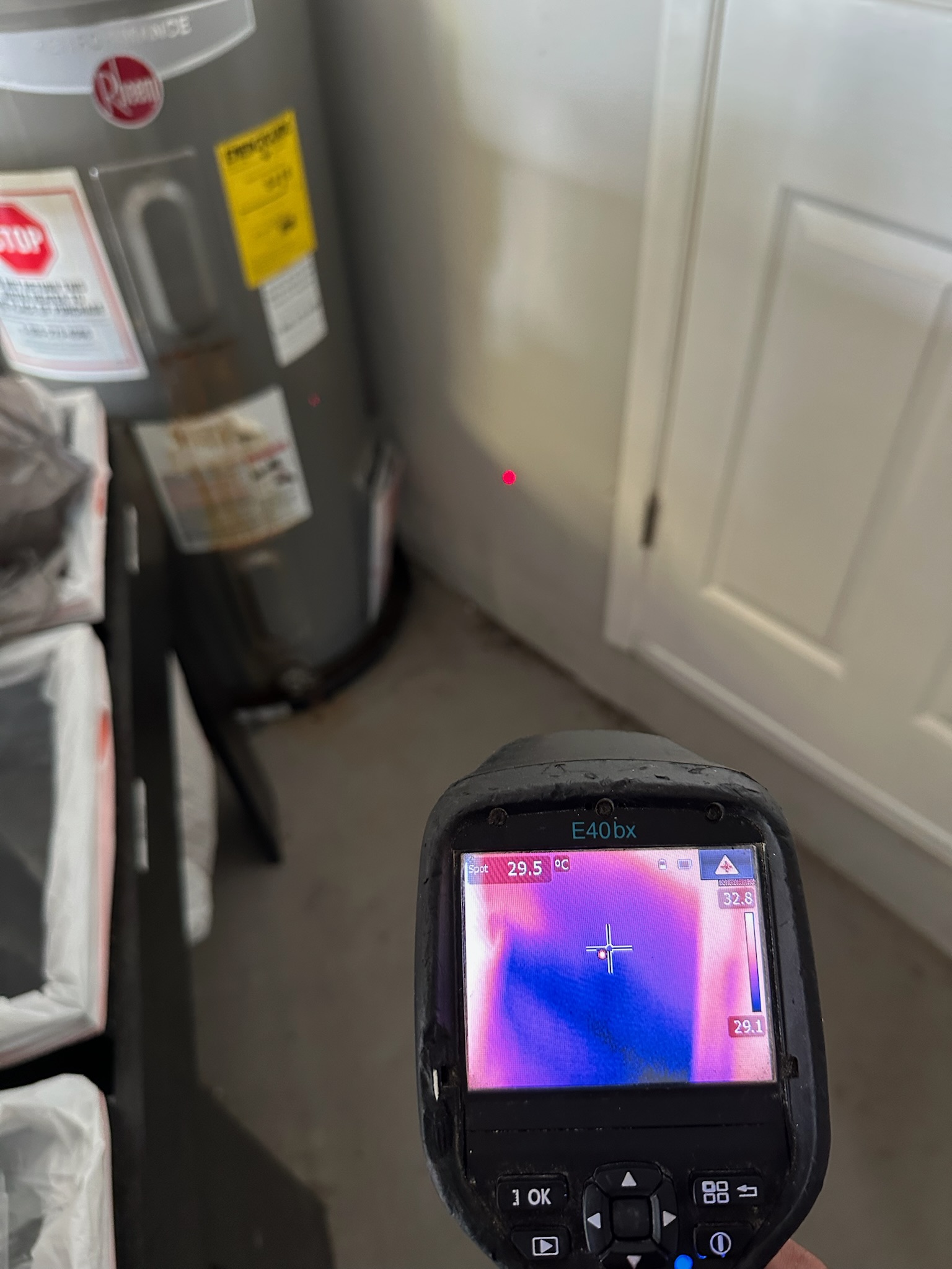 Infrared camera reveals a dark blue moisture patch on the garage wall near the water heater during a Palm Harbor leak detection job.