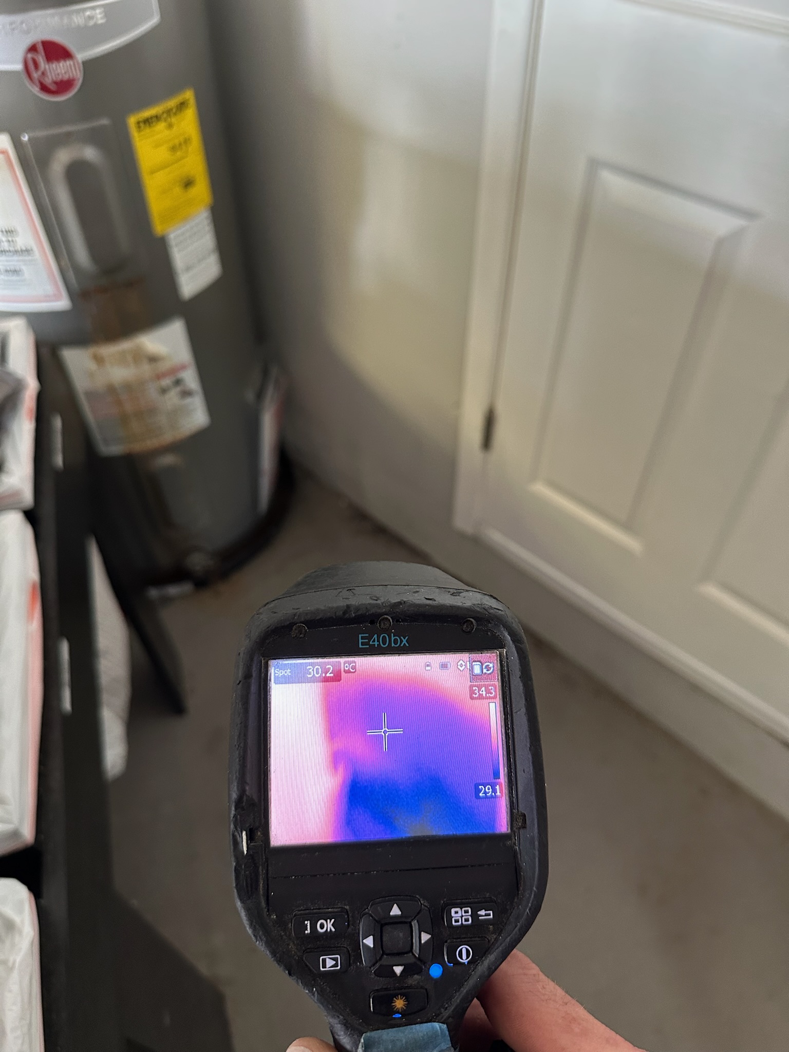 Tyler uses a FLIR infrared camera to inspect for hidden leaks behind a water heater in a Palm Harbor garage.
