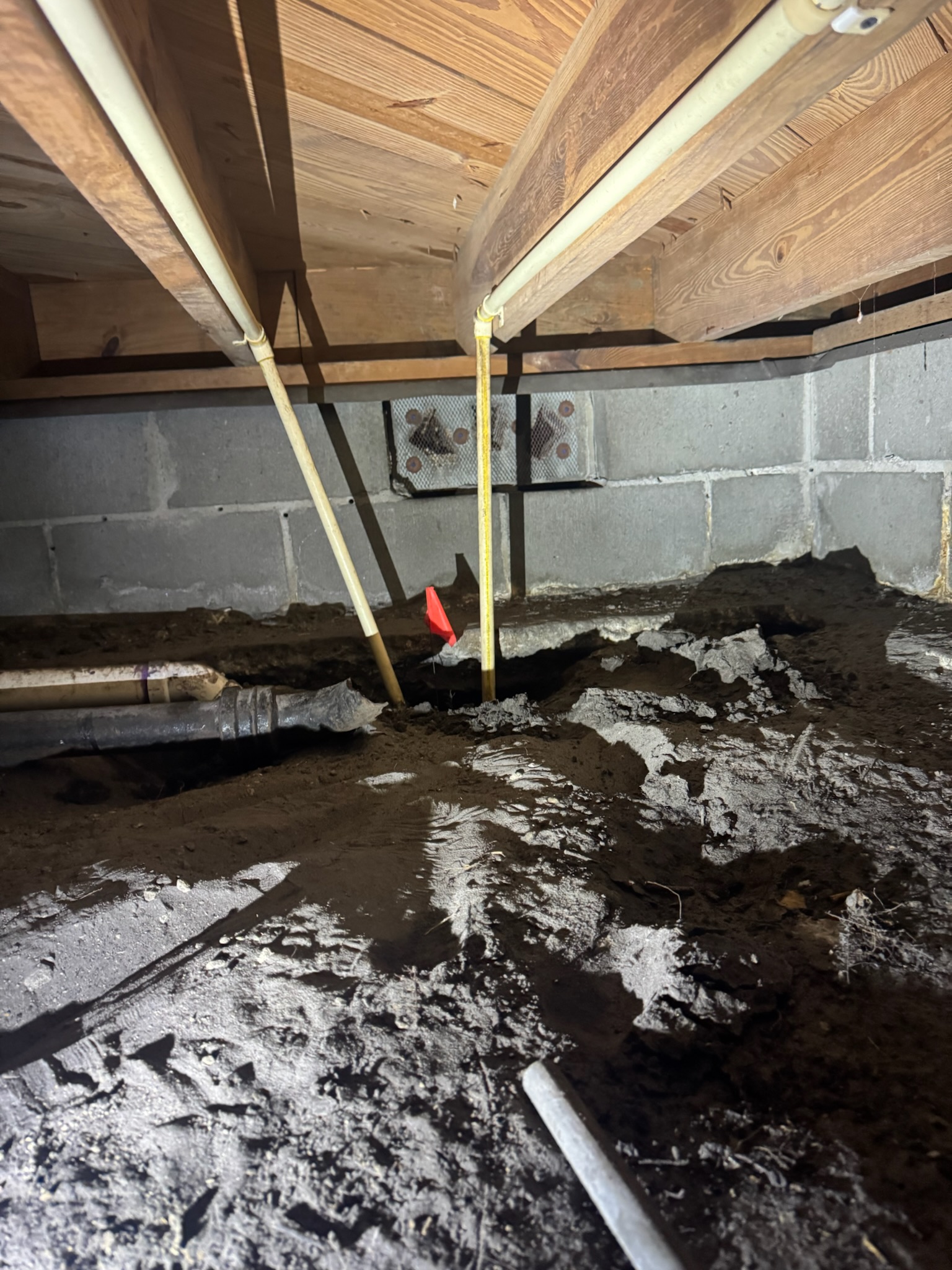Close-up view under house showing pipes going underground with flashlight and orange flag