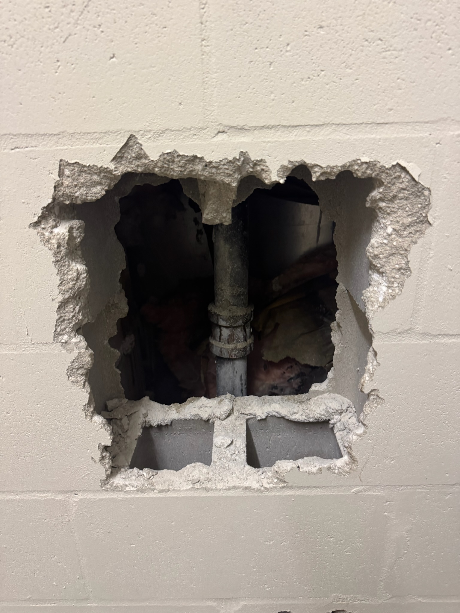 Galvanized fire line visible behind a square hole in a Clearwater condo block wall after leak detection