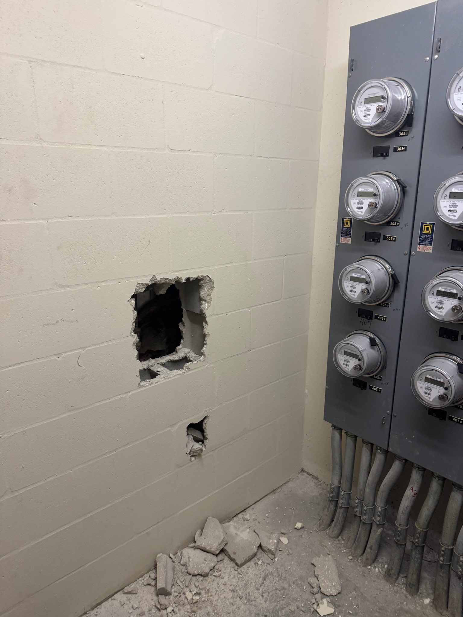 Concrete rubble and a square hole in a block wall near power meters where a leak was confirmed in a Clearwater condo