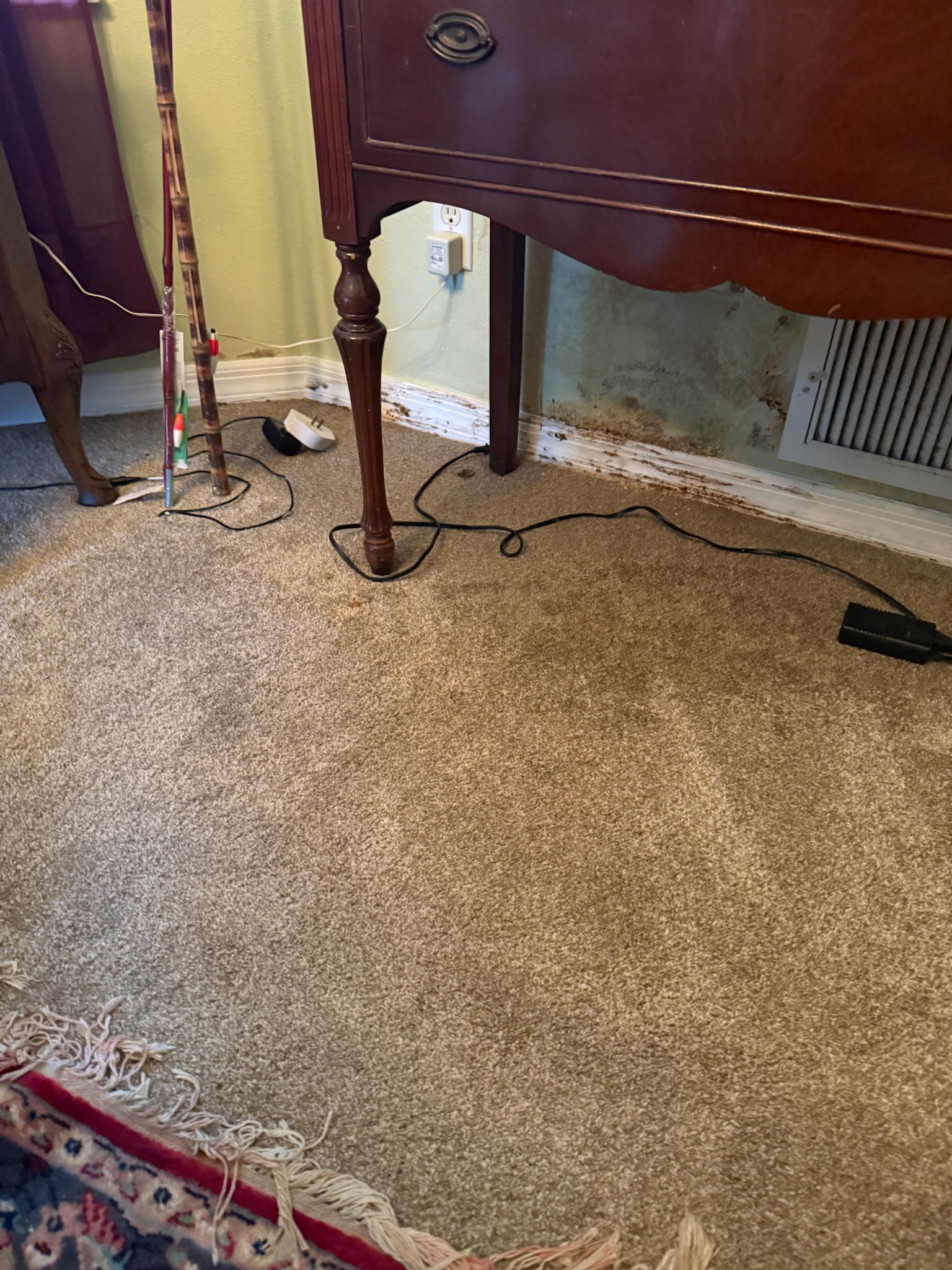 Hidden moisture damage on wall and baseboards beneath furniture near an air conditioning grate