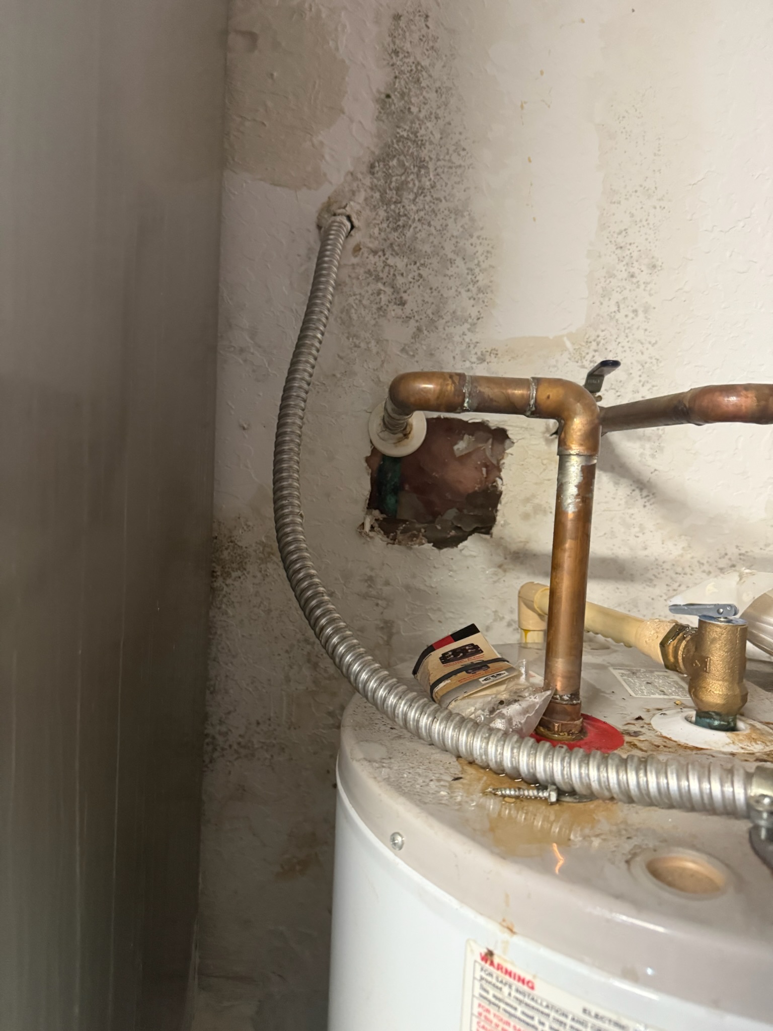 Targeted wall opening exposing a copper pipe leak behind a water heater