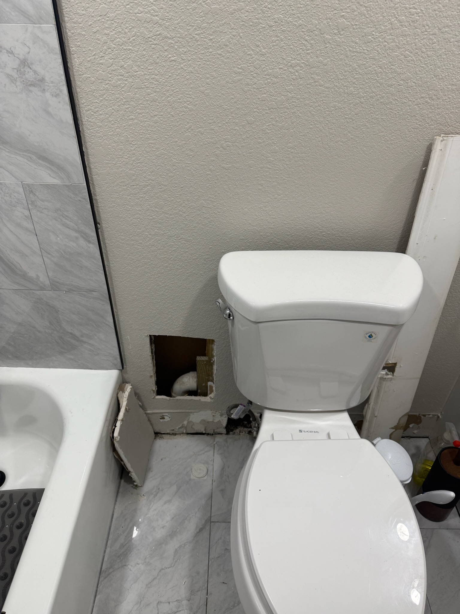 Bathroom in a St. Petersburg home with baseboard removed and wall openings behind the toilet during a water leak investigation.