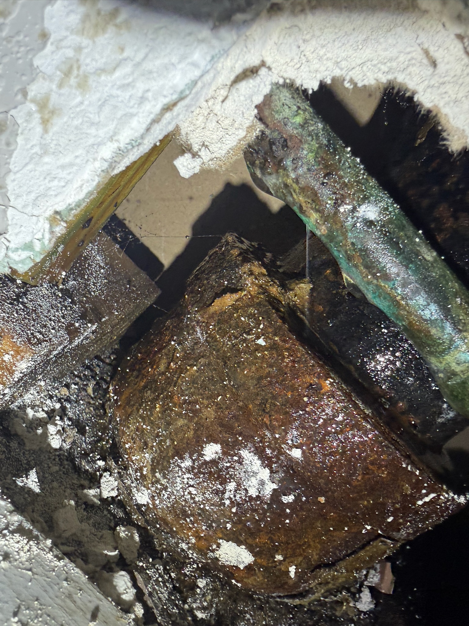 Close-up of a deteriorated copper pipe pinhole leak spraying onto a cast iron stack inside a St. Petersburg bathroom wall.