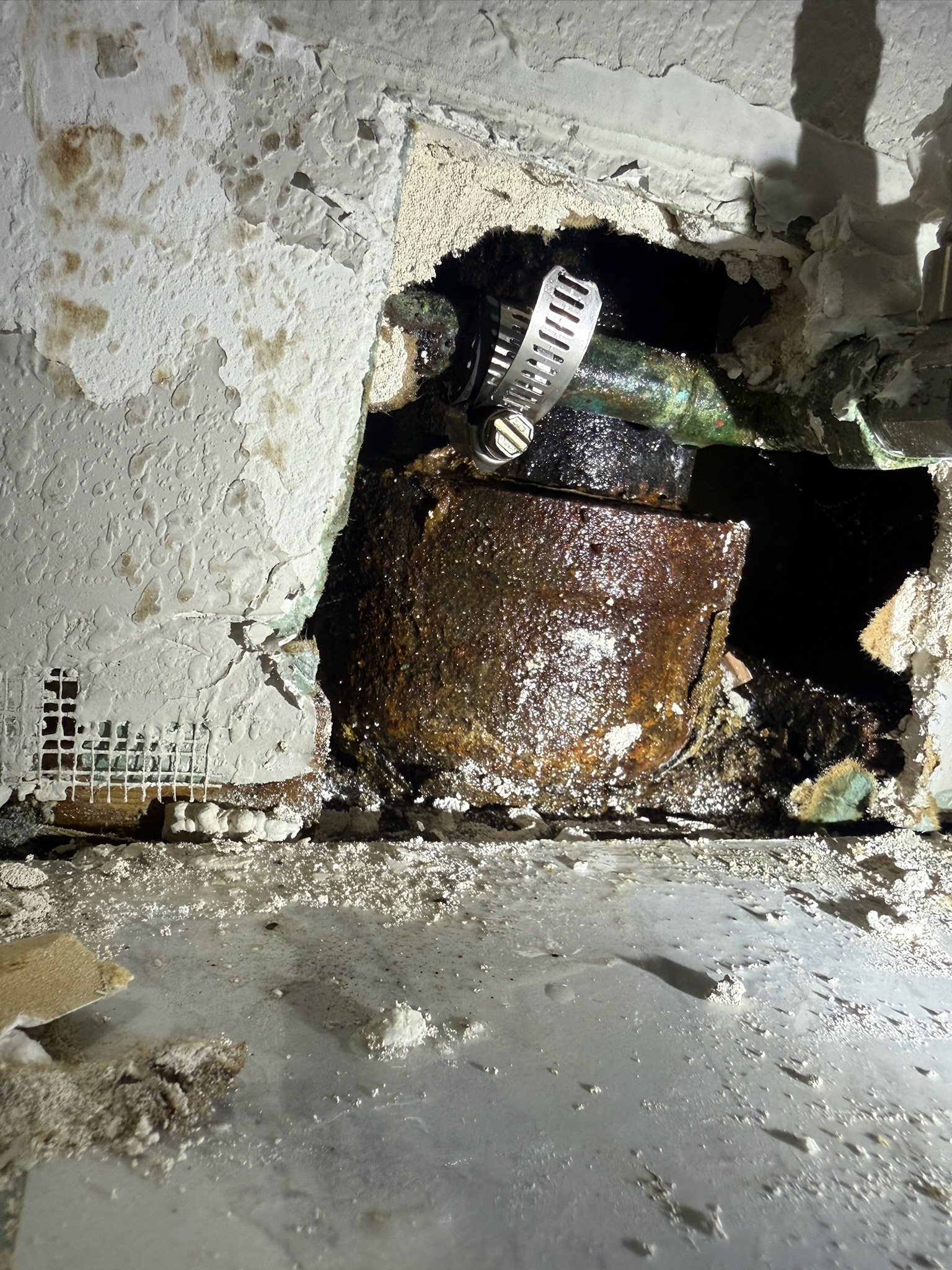 Temporary rubber and hose clamp placed over a copper pipe pinhole leak inside a St. Petersburg bathroom wall.