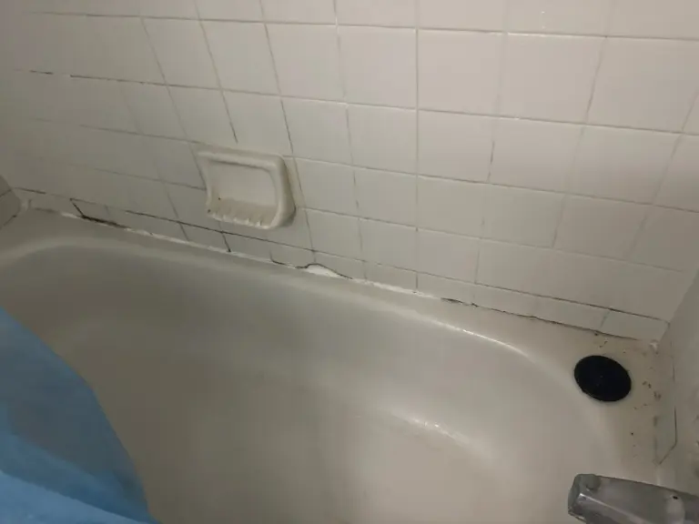 White bathtub below a white tile wall with a built-in soap dish.