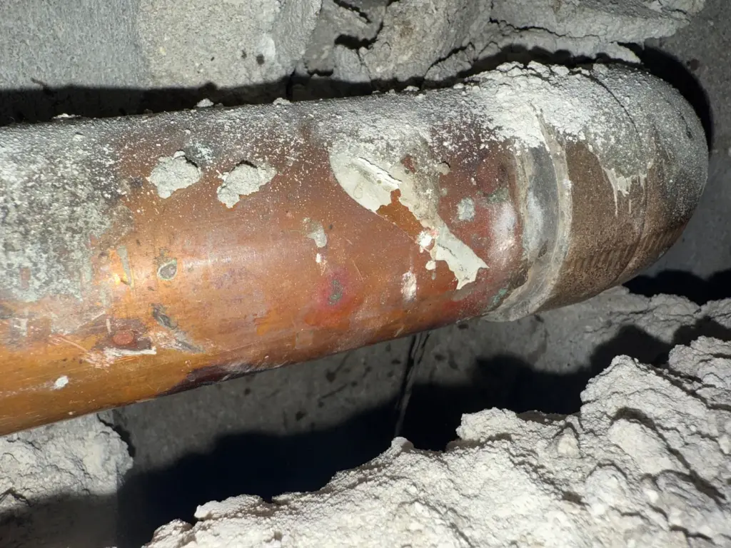 Close-up of a copper pipe and joint discolored with corrosion and patches of white mineral deposits.