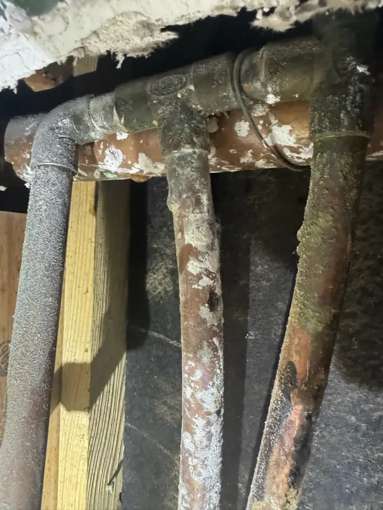 Corroded copper water pipes and fittings with white mineral deposits inside an opened wall.