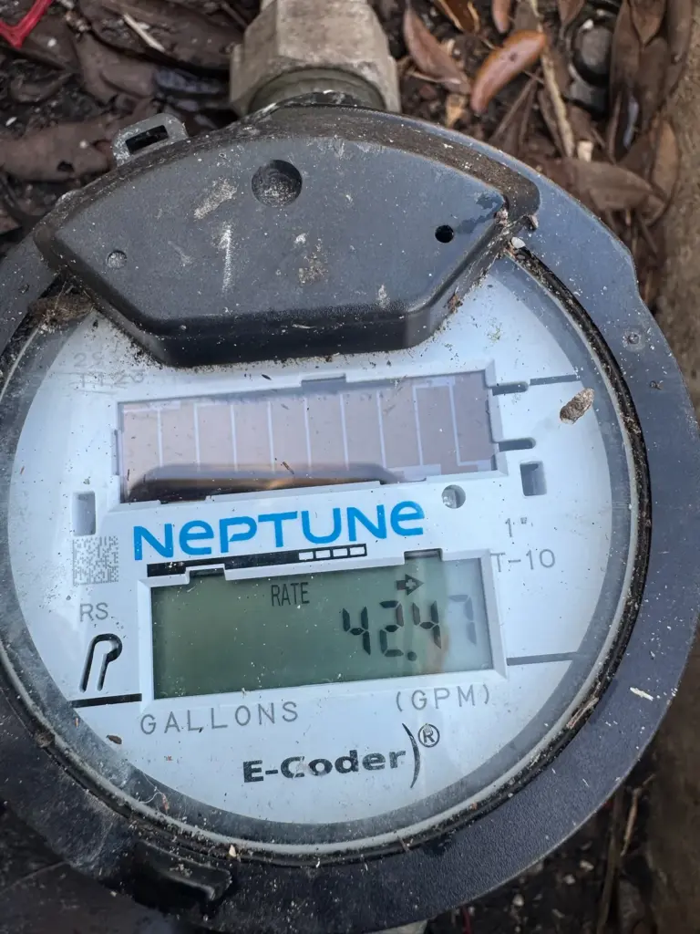 Close-up of a digital water meter face showing a gallons reading, inside a ground box.
