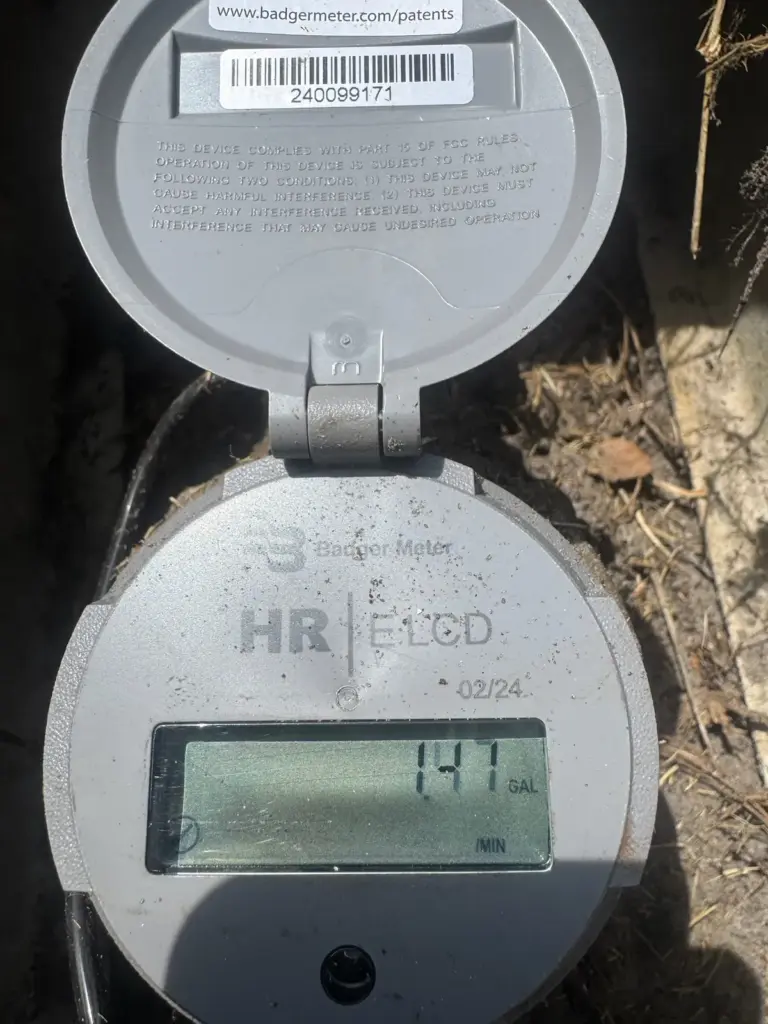 A digital water meter with its hinged lid open shows a reading on its display.