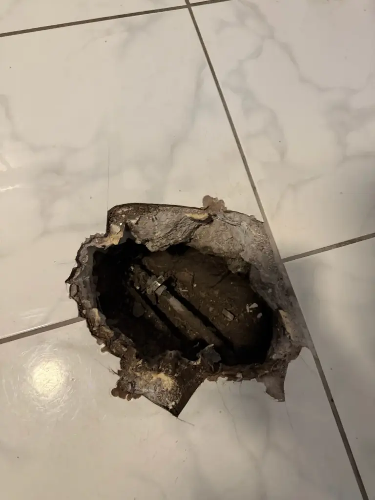 A ragged hole cut through glossy marble-look floor tile exposes the concrete slab and soil below.
