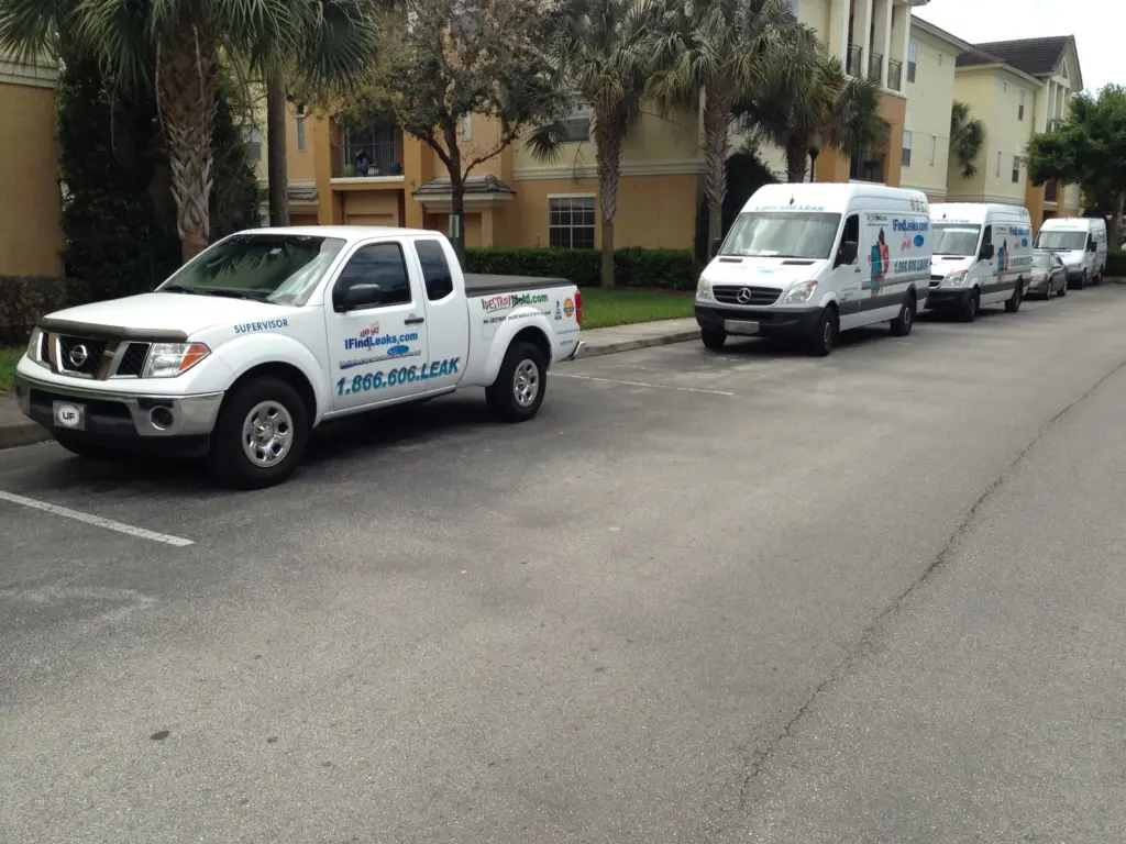 White I Find Leaks supervisor pickup and three branded service vans parked in a row at an apartment complex.