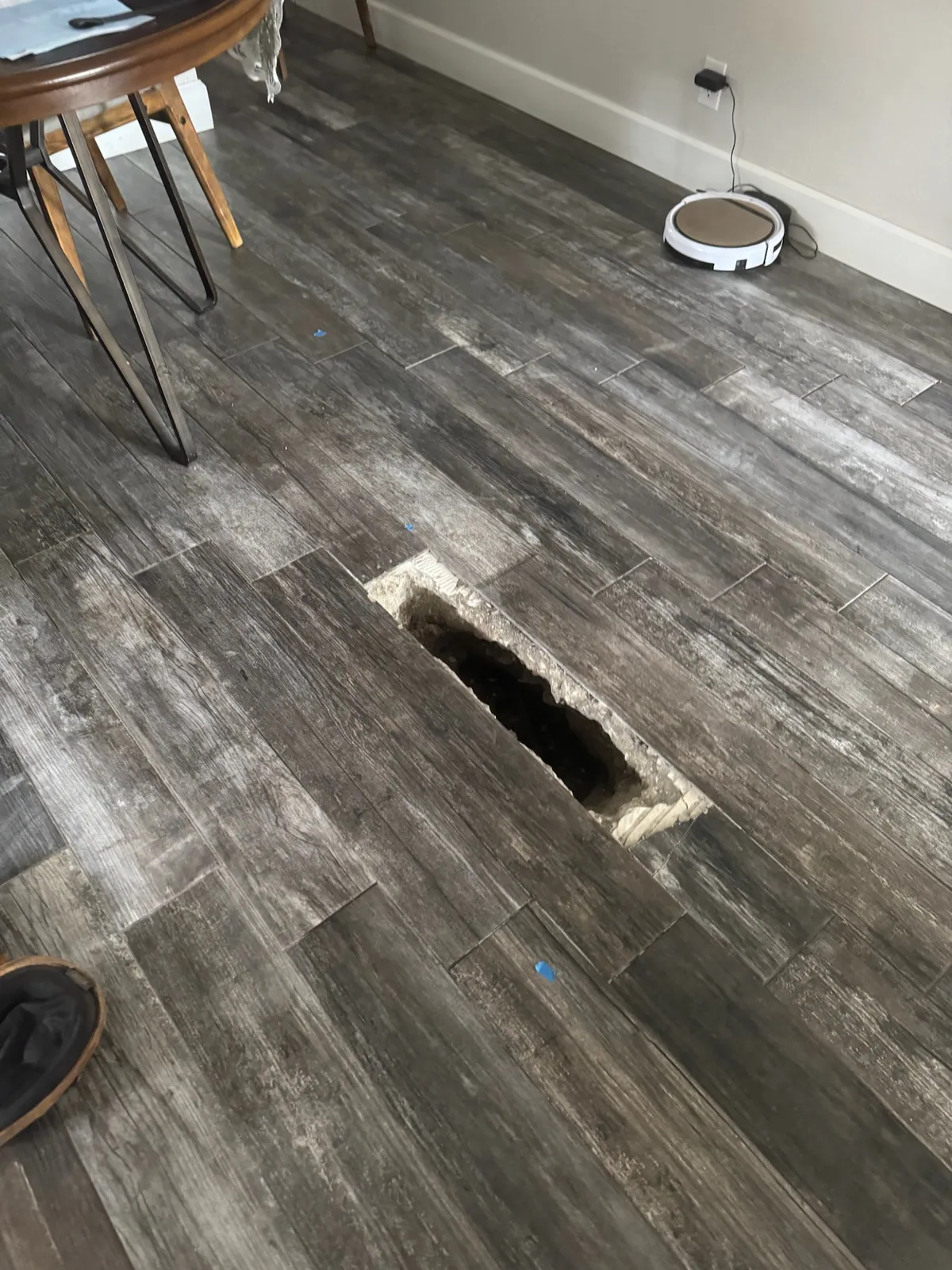 Narrow rectangular opening cut through a dark wood-look tile floor and the slab beneath it.