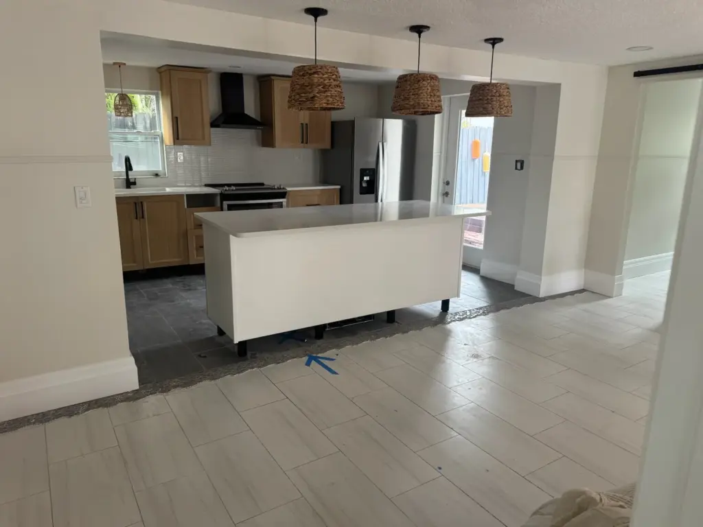 Open kitchen with a white island and pendant lights, with a blue tape arrow on the floor pointing to the island.