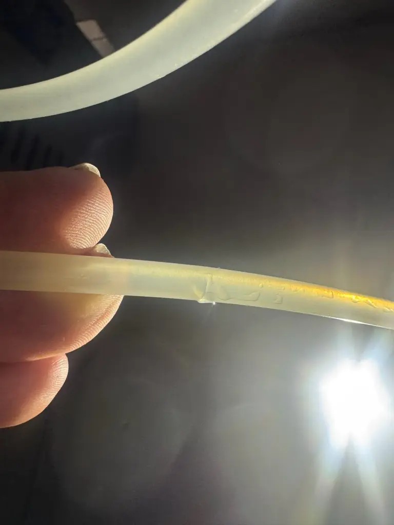 Fingers holding a thin plastic water supply tube with a small split and a bead of water, lit by a flashlight.