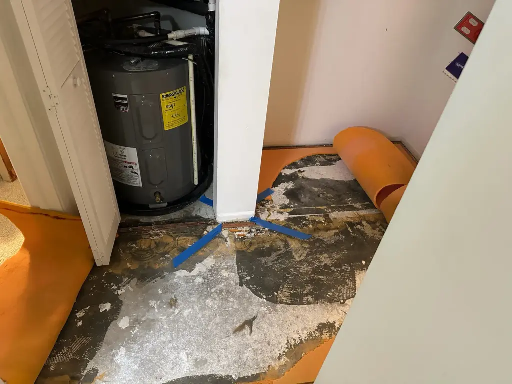 Blue tape mark on bare stained concrete where carpet was pulled back, in front of a water heater closet.