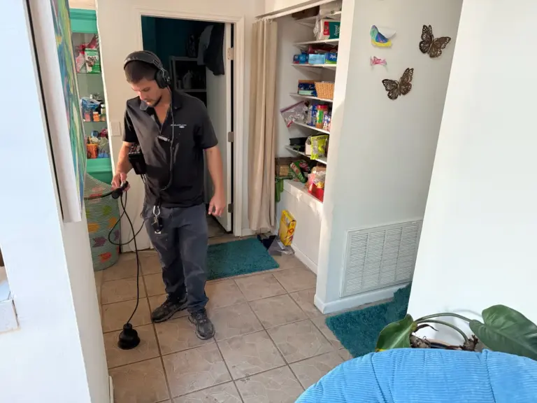 Technician wearing headphones listens through an acoustic ground microphone on a tile hallway floor.