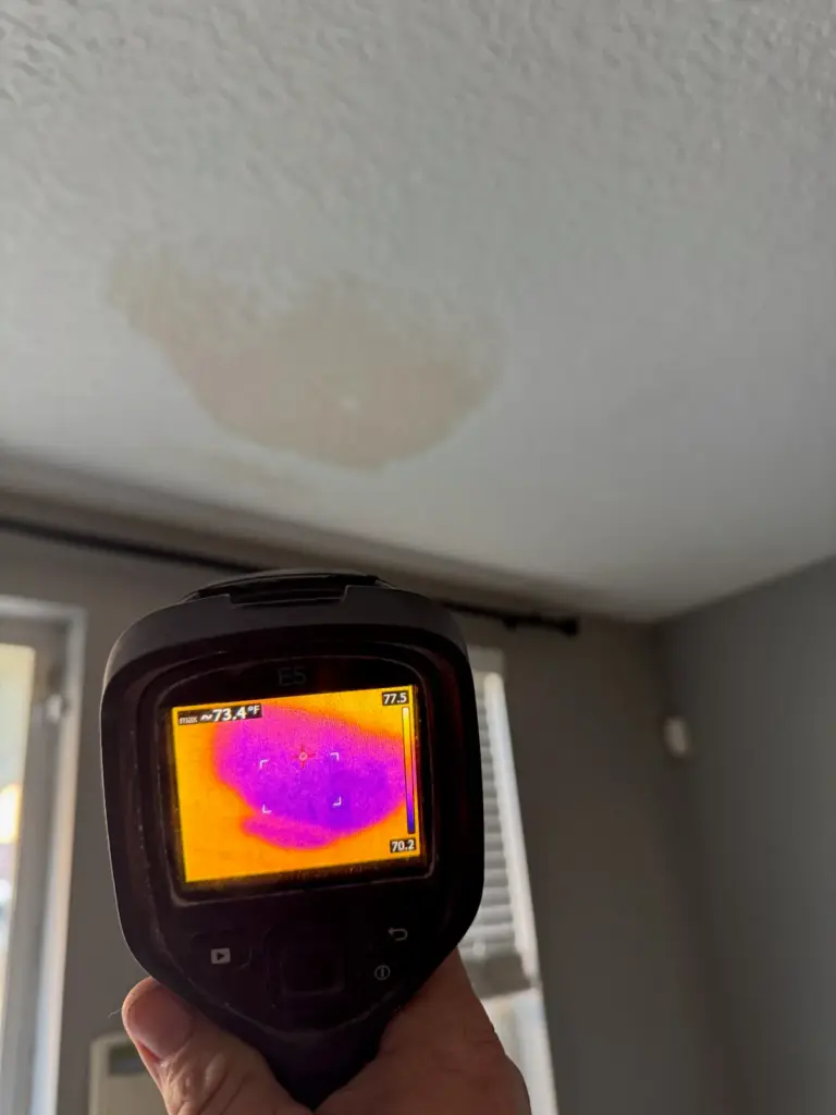 Thermal camera aimed at a brown water stain on a textured ceiling, its screen showing a purple cool area.