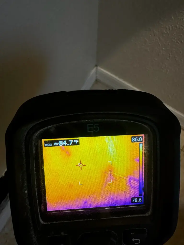 Thermal camera aimed at a wall corner, its screen showing a yellow and orange warm image.