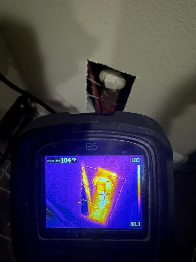 A thermal camera aimed at a narrow wall opening shows a hot yellow pipe fitting against cooler purple surroundings.