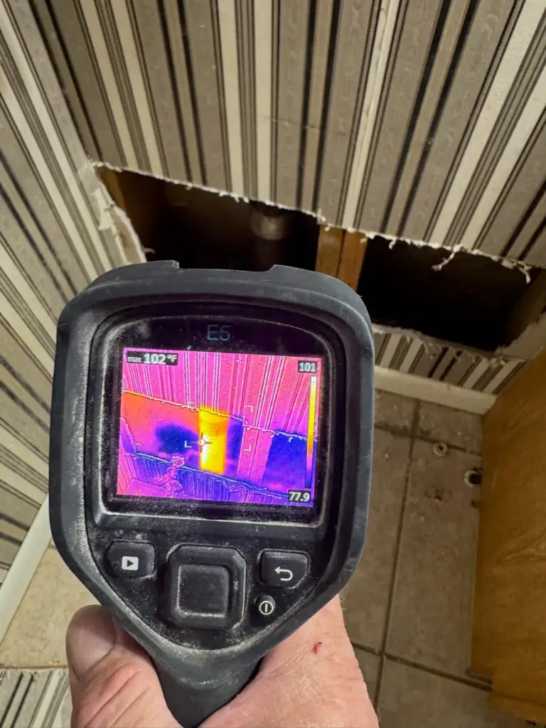 A thermal camera screen showing a bright yellow hot streak where a section of striped wall has been cut open.