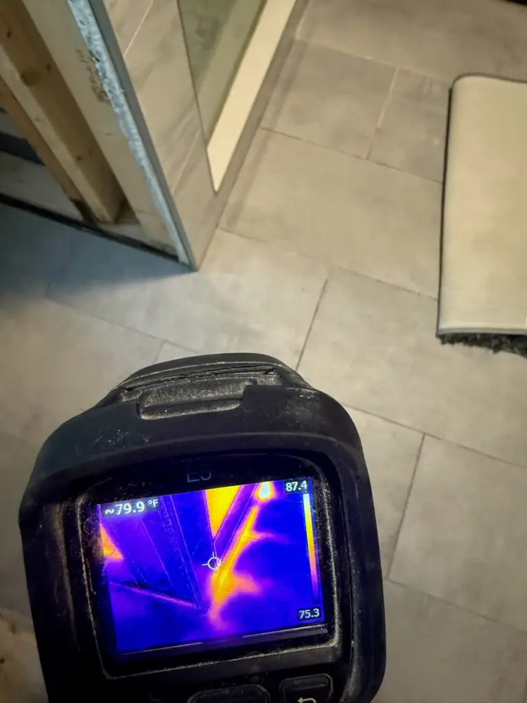 Thermal camera screen showing bright branching lines on a tiled bathroom floor beside a shower door.