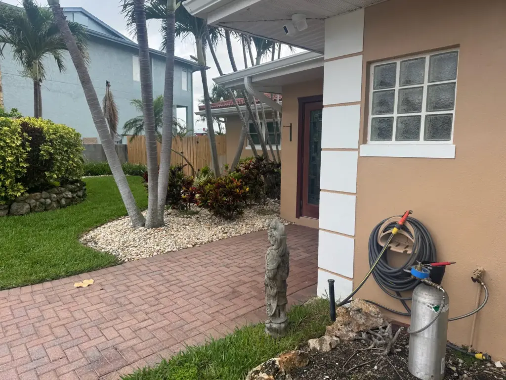 Front entry with a brick paver walkway and a gas cylinder connected by hose at an outdoor spigot.