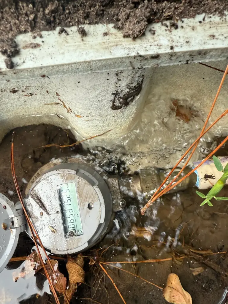 Water bubbling and flowing around a digital water meter inside a flooded in-ground meter box.