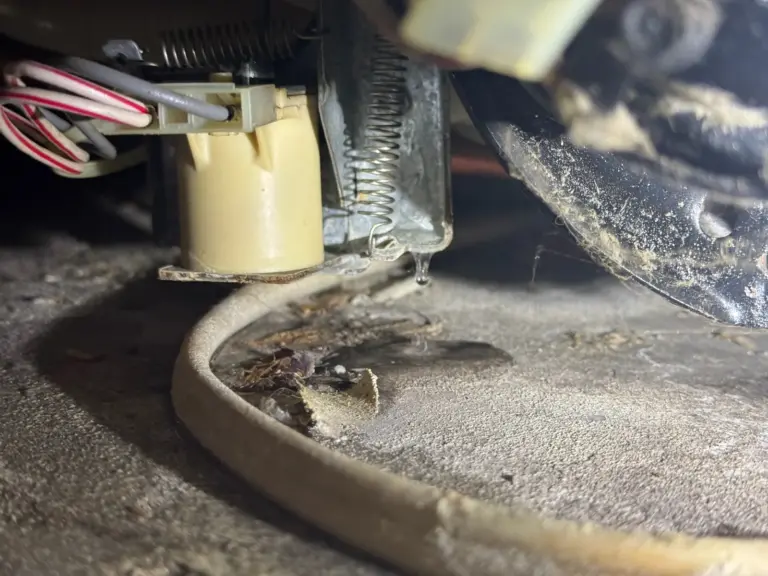A drop of water forms beneath a small water valve with wires attached, under an appliance.